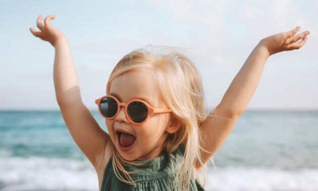 Funny kid girl playing outdoor surprised emotional child in sunglasses 3 years old baby raised hands