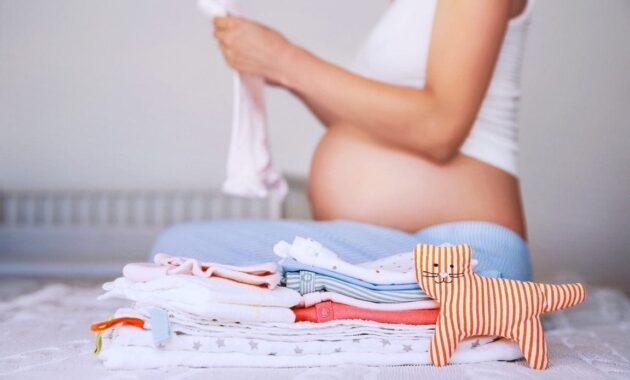 Pile of baby clothes necessities and pregnant woman on bed in home interior of bedroom. 827772708 12.jpeg