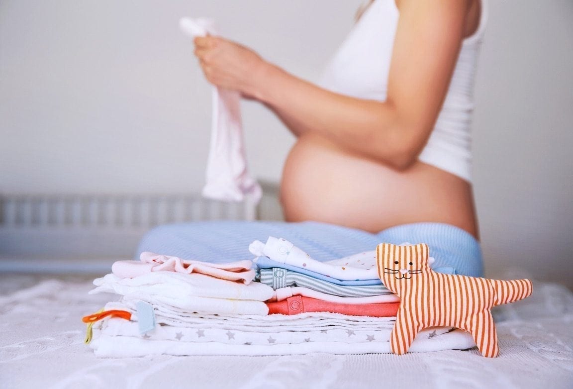 Pile of baby clothes necessities and pregnant woman on bed in home interior of bedroom. 827772708 12.jpeg